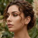 Woman wearing a curated ear stack with 14K gold daith, helix and lobe jewelry.